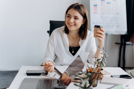 A Happy Woman Sitting on the Swivel Chair while Holding a Cup of Coffee