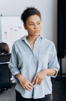 Portrait of a young woman with afro hair standing in an office, looking contemplative.