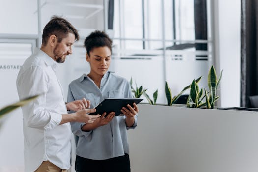 Two coworkers discussing work using a tablet in a modern office setting.