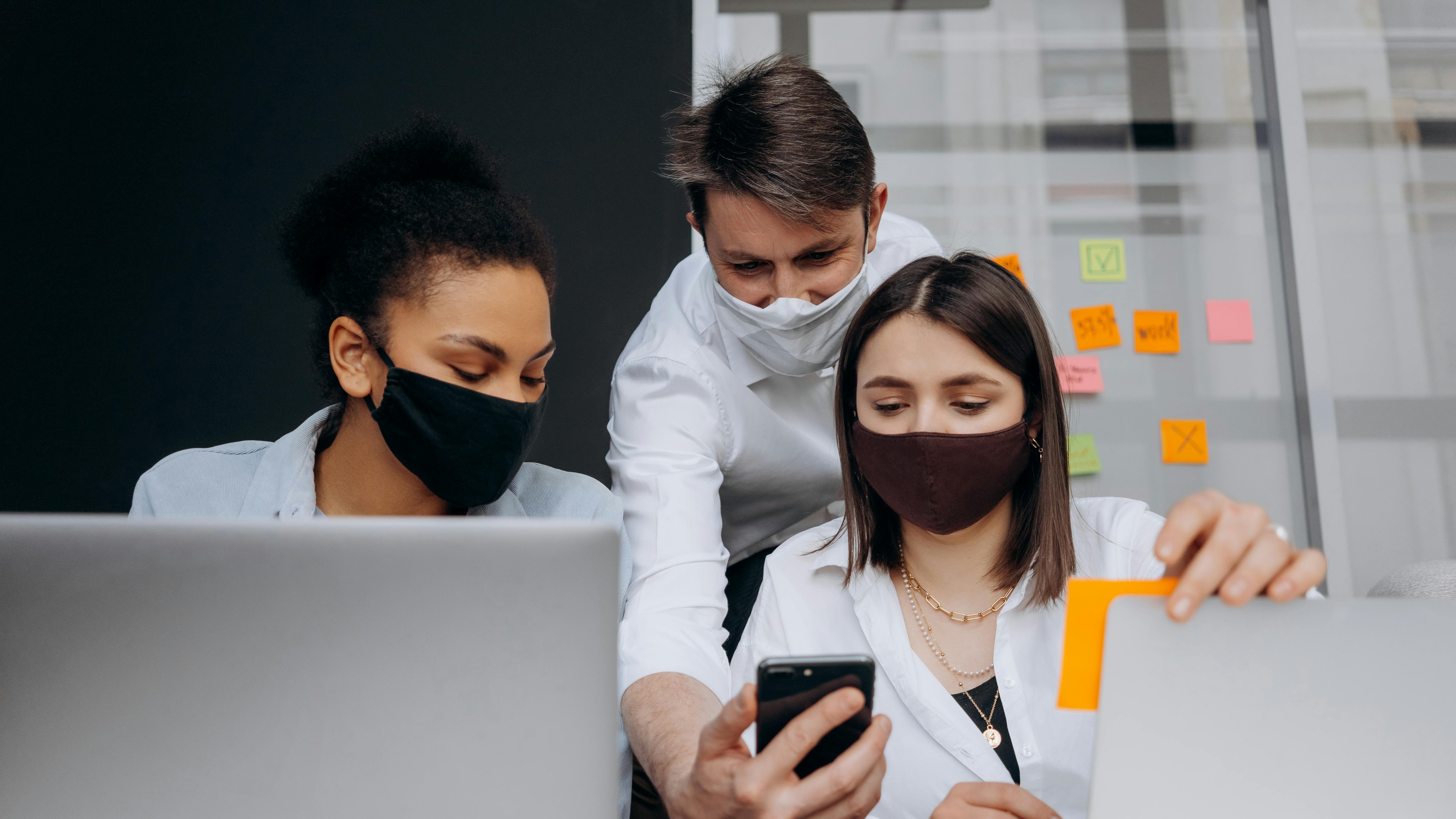 group of people wearing face masks looking at a smartphone