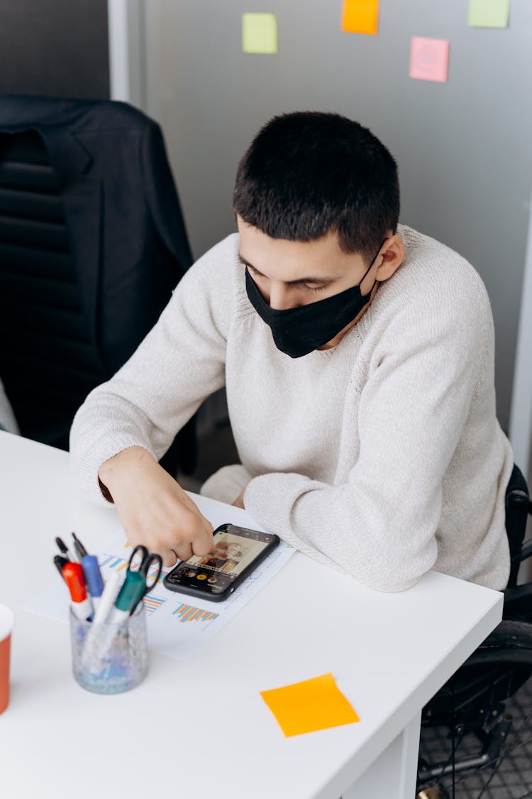 Man Wearing A Face Mask Using A Smartphone On A White Table