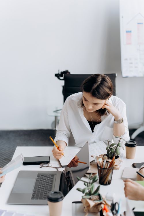Free Woman in a white shirt working intently at a desk with laptop, notes, and coffee. Stock Photo