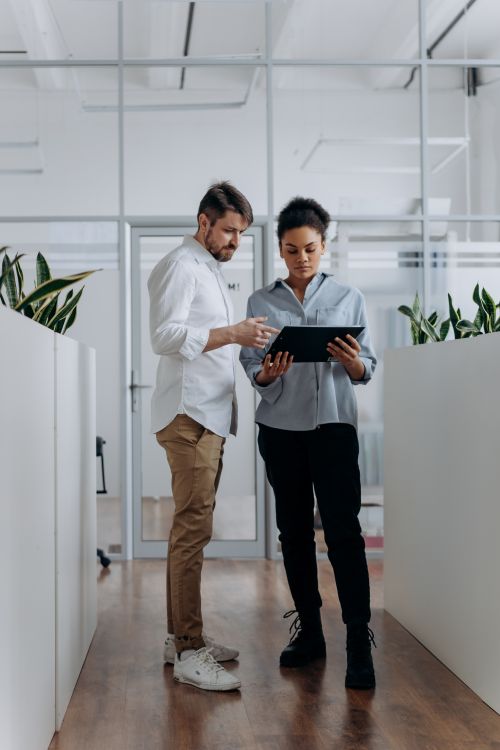 Free Two professionals discussing work on a tablet in a modern office hallway. Stock Photo
