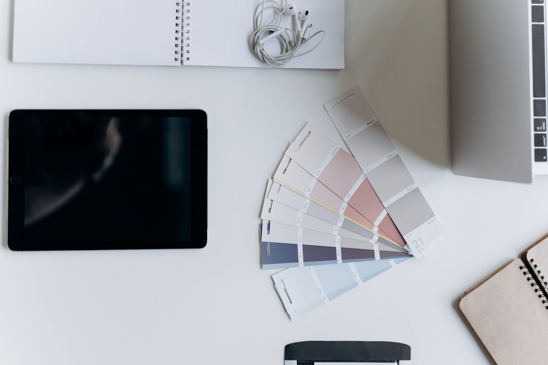 Flatlay of a modern minimalist workspace featuring tech gadgets and color swatches on a white surface.