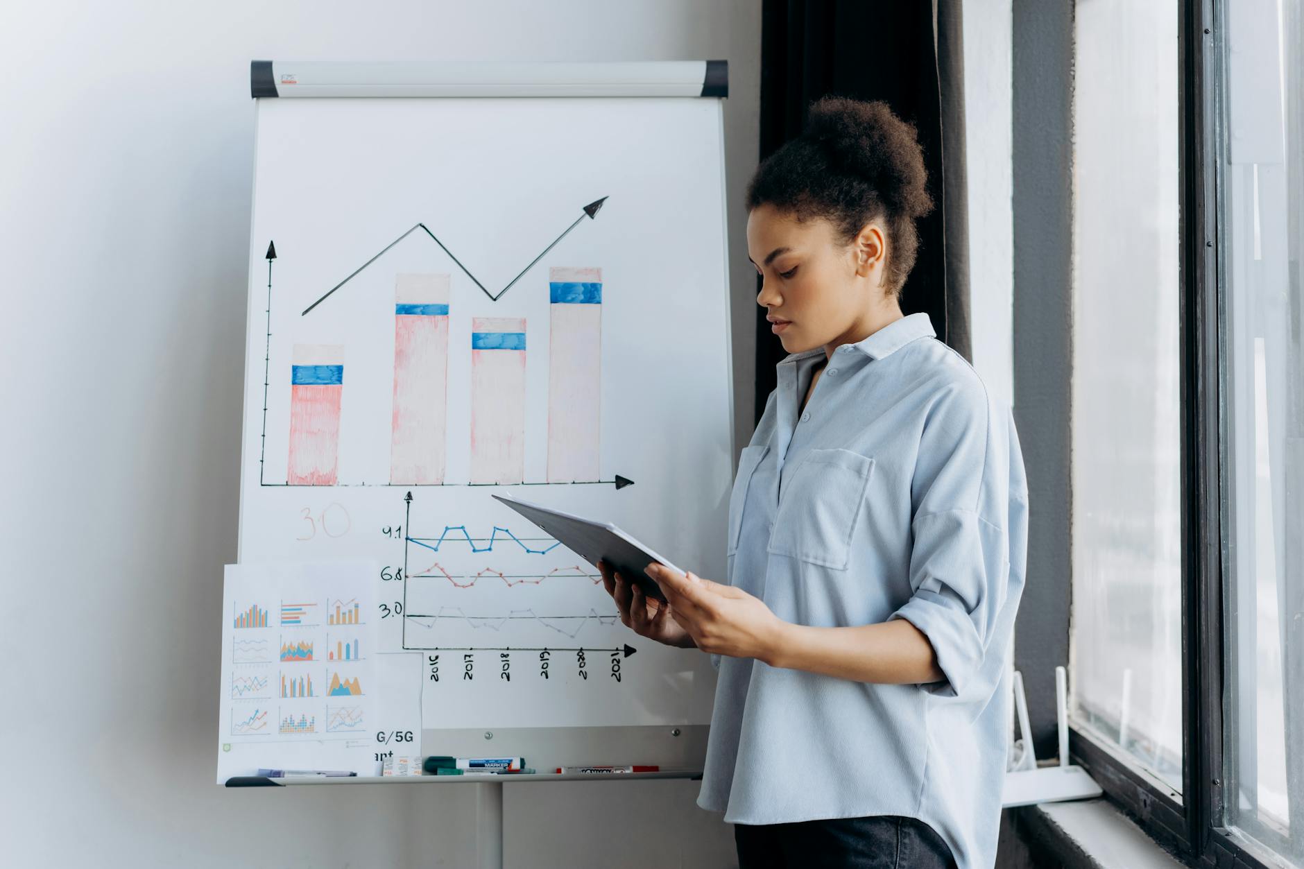 A woman analyzing sales data on a tablet next to a board with graphs, symbolizing business-focused technology metrics.
