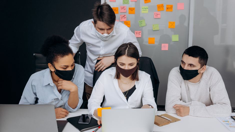 A diverse group of colleagues collaborating in an office while wearing face masks.