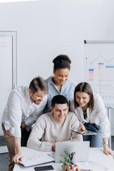 Diverse team of adults collaborating around a laptop in a modern office setting.