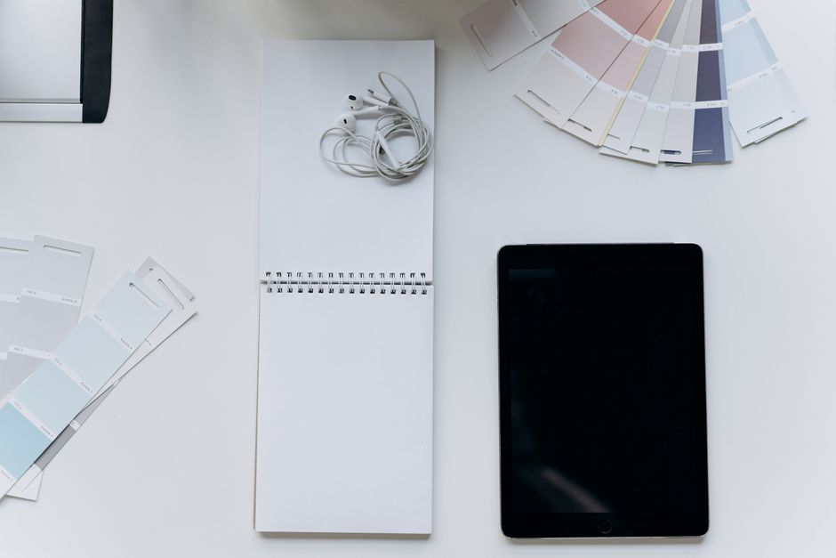 Top view of a flat lay with earphones, notepad, tablet, and color swatches for design inspiration.