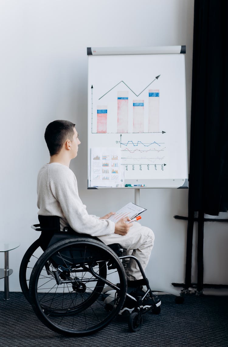 A Man Sitting On The Wheelchair While Looking At The Graph On The Board