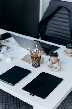 A well-organized workspace featuring a laptop, notebooks, and coffee cups on a white desk.