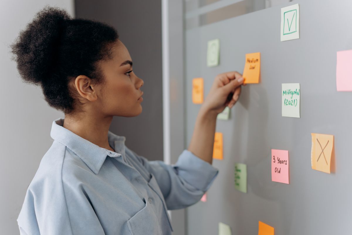 Woman sorting colour-coded sticky notes marked with ticks and crosses on a board
