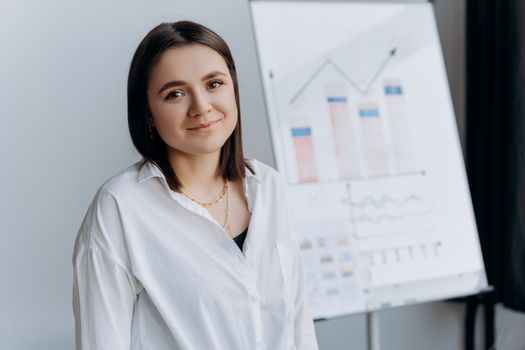 Smiling woman in a white shirt presents business graphs on a flipchart in a modern office.
