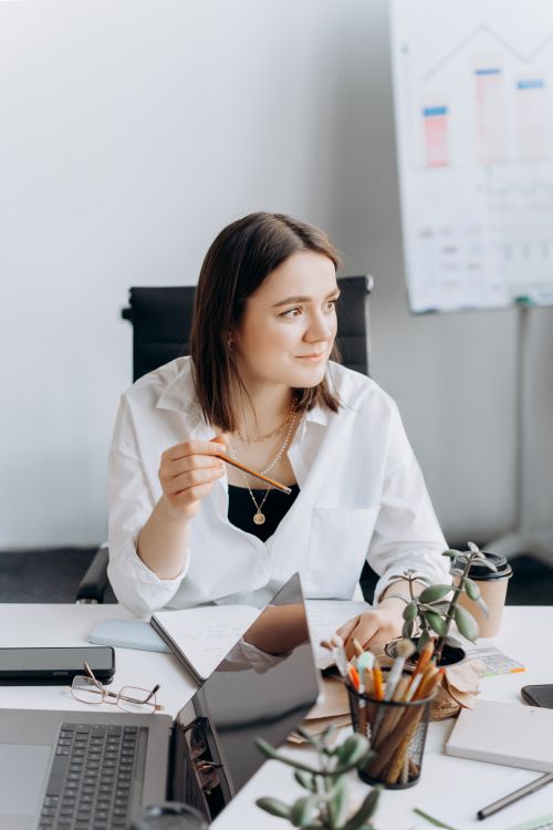 Free Businesswoman sits thoughtfully at desk with laptop and notes, projecting success and focus. Stock Photo