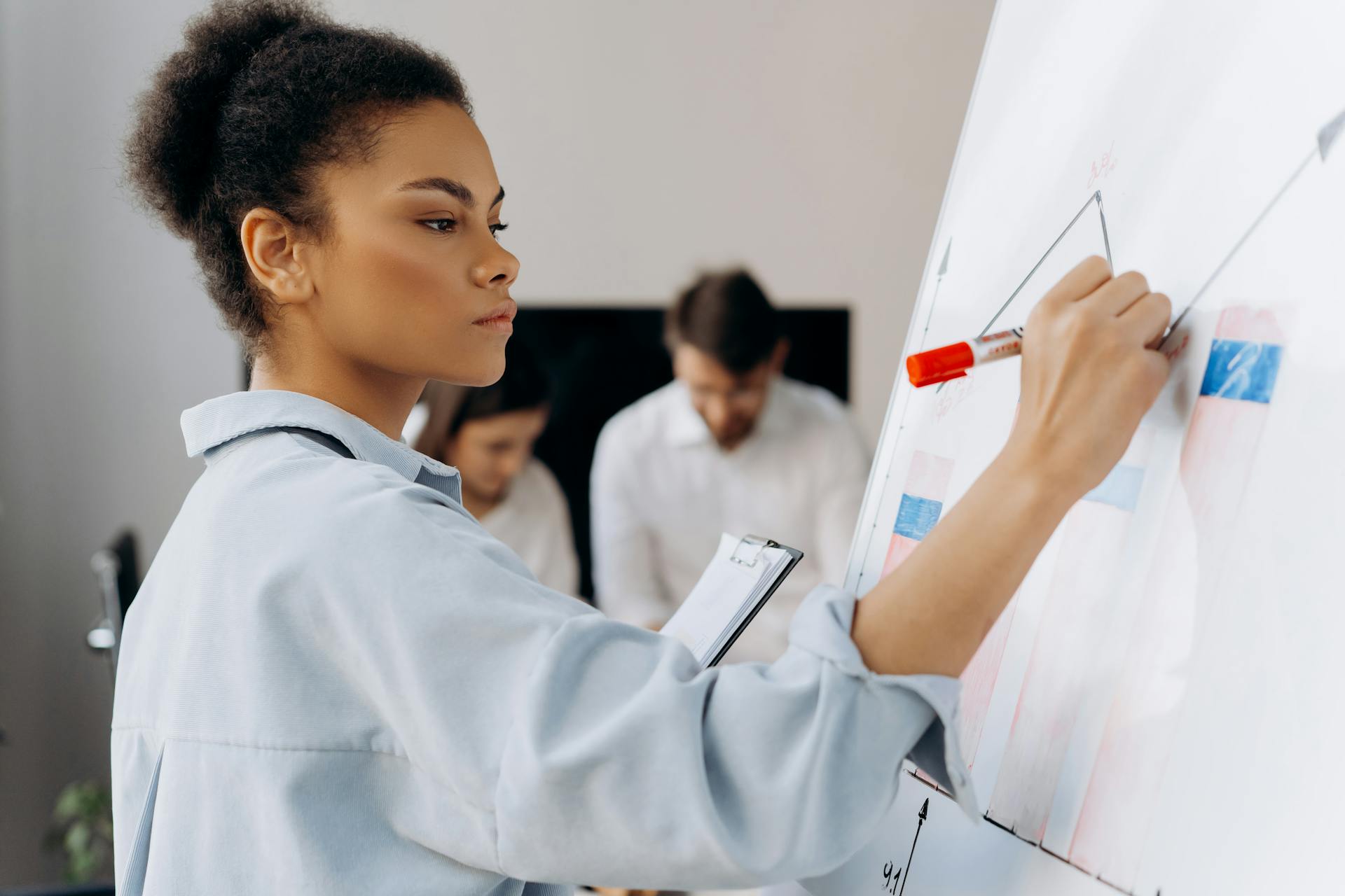 Confident businesswoman illustrates data on whiteboard during a team meeting, showcasing collaborative analysis.