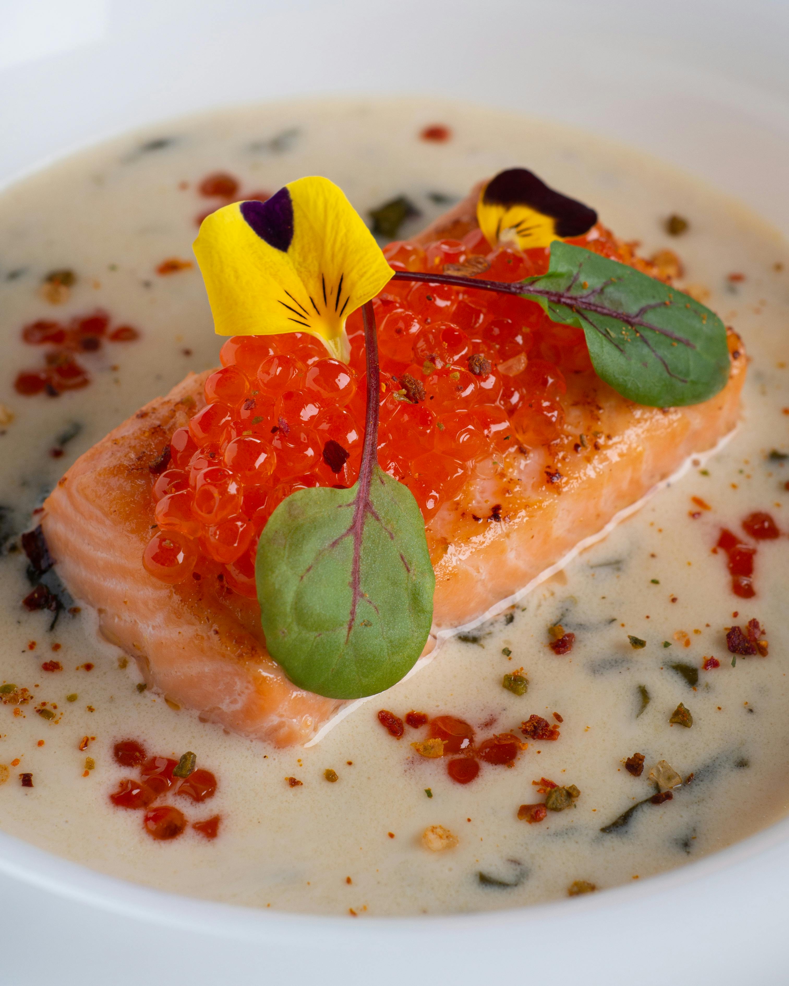 A delectable salmon dish topped with roe and garnished with edible flowers, perfect for seafood lovers.