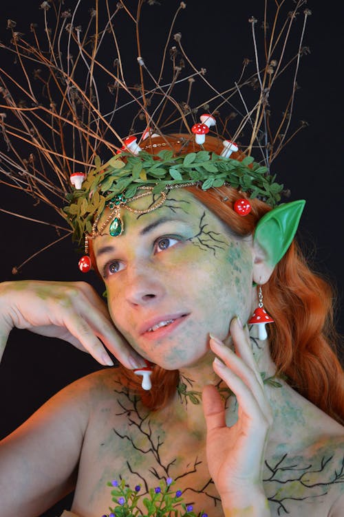 Portrait of fanciful young female with elven makeup and pointy green ears wearing circlet of plants and amanita accessories on head