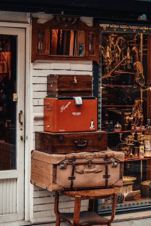 Free Stack of vintage luggage outside an antique store with ornate decor and reflection in window. Stock Photo