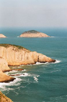 A breathtaking aerial view of rocky cliffs and small islands in a calm ocean under a clear blue sky.