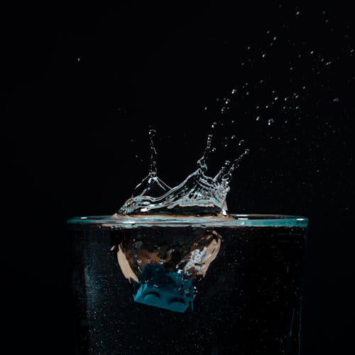 Small blue constructor detail falling in glass with clear water making splashes and drops on black background