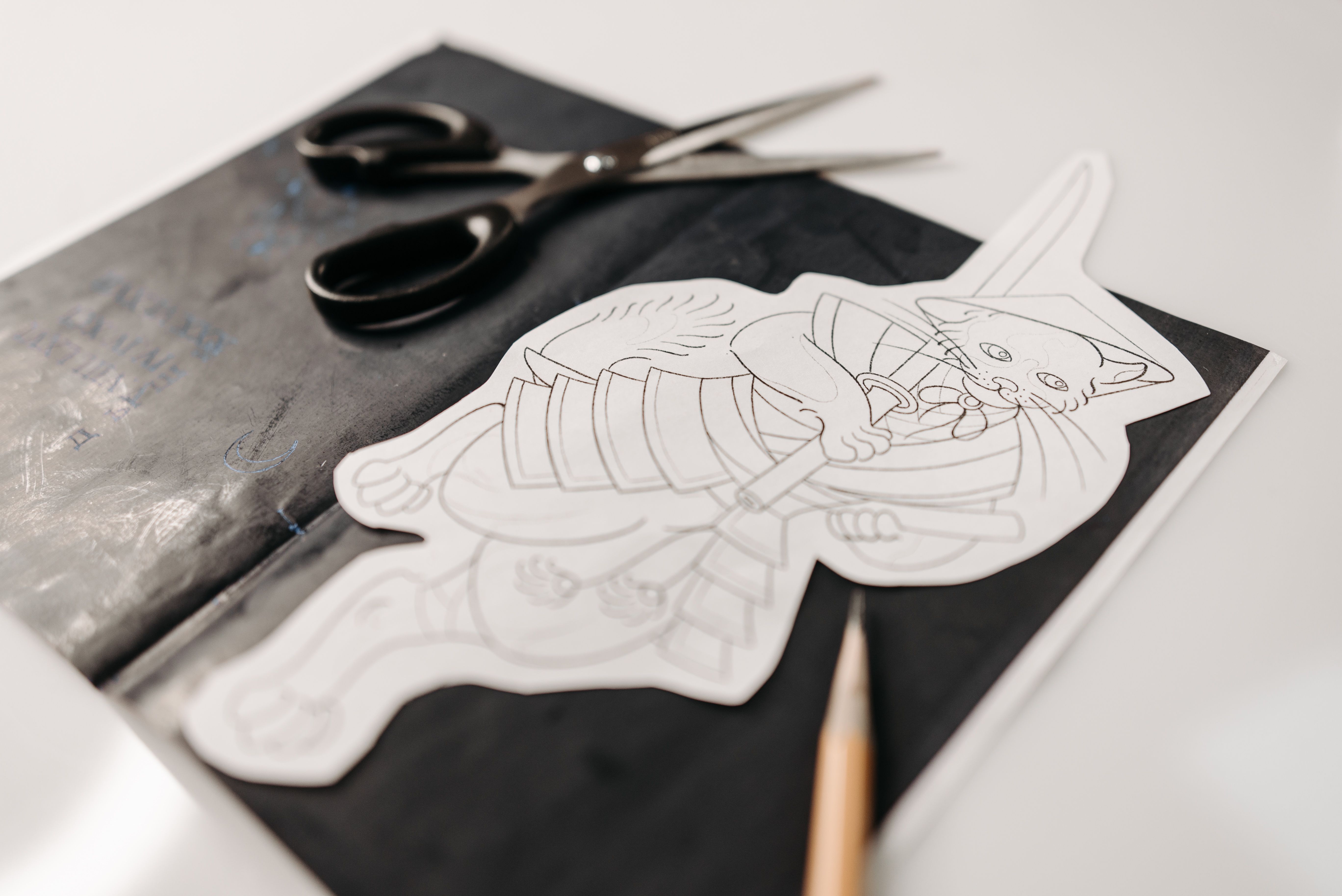 Artistic photo featuring a cat drawing with scissors and pencil on a black surface.