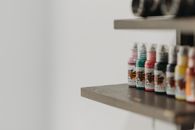 Close-up of colorful tattoo ink bottles neatly arranged on a wooden shelf, ideal for a tattoo parlor setting.
