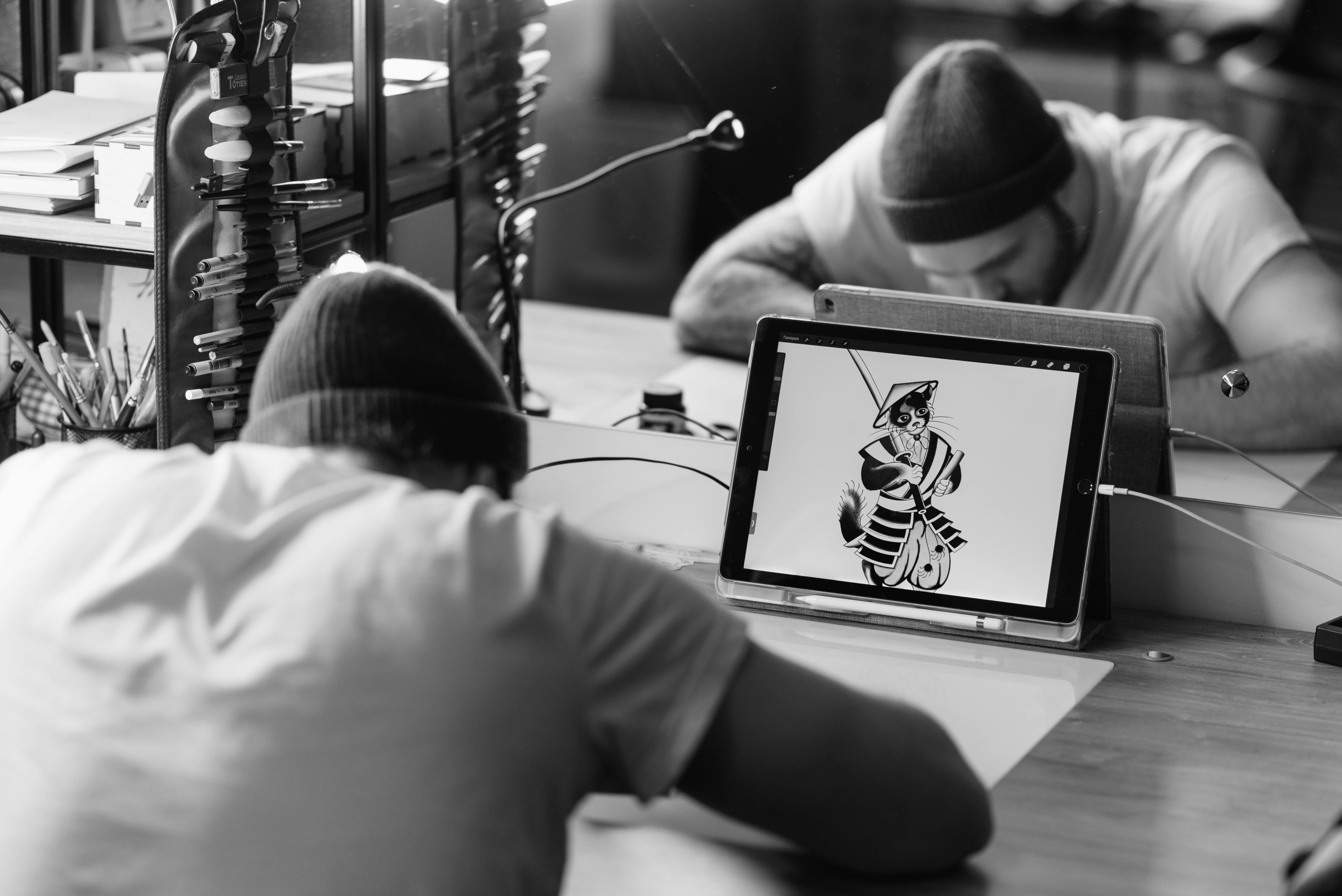 Black and white photo of a tattoo artist working on a digital design in a tattoo parlor.