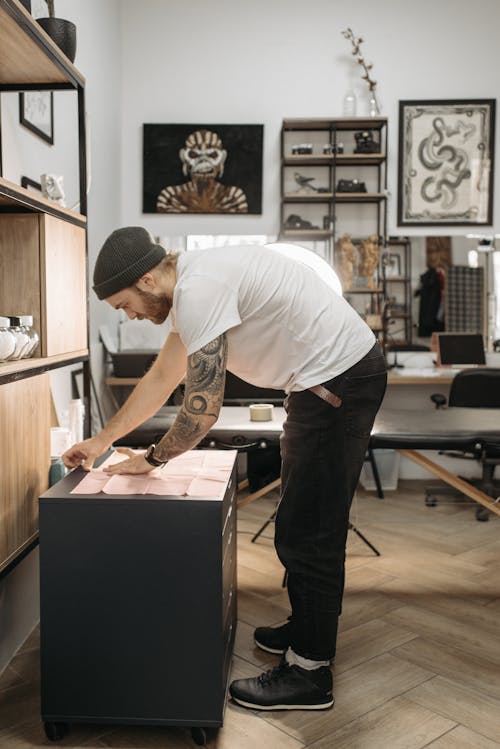 A Man in White Shirt Putting the Pink Paper on Top of a Wooden Drawer