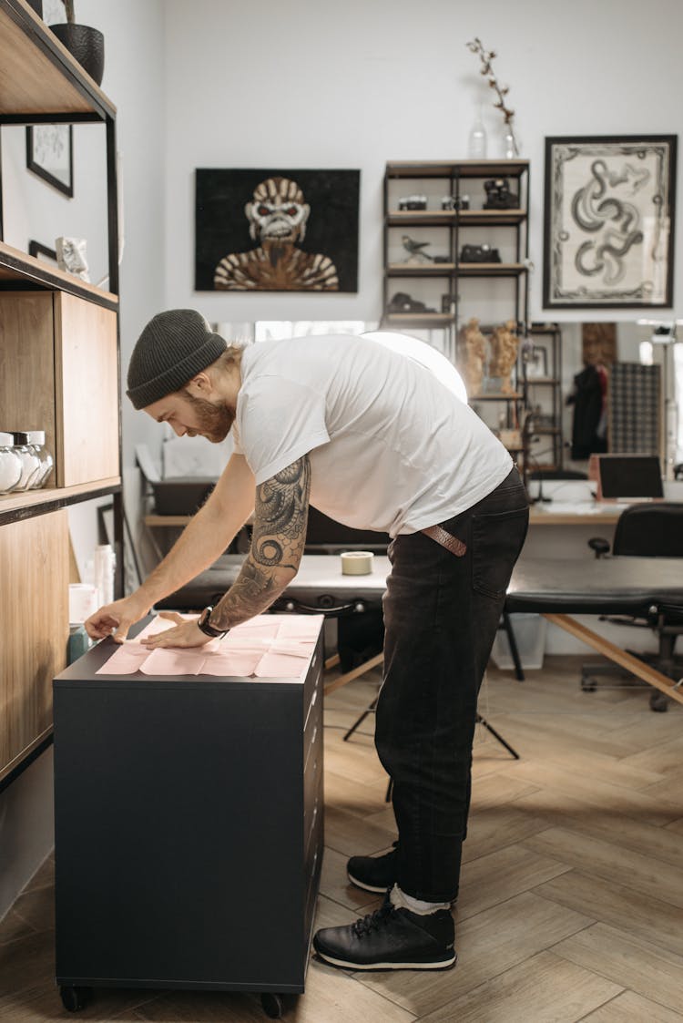 A Man In White Shirt Putting The Pink Paper On Top Of A Wooden Drawer