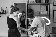 Tattoo artist concentrates on creating a detailed design on a client's arm in a studio setting.