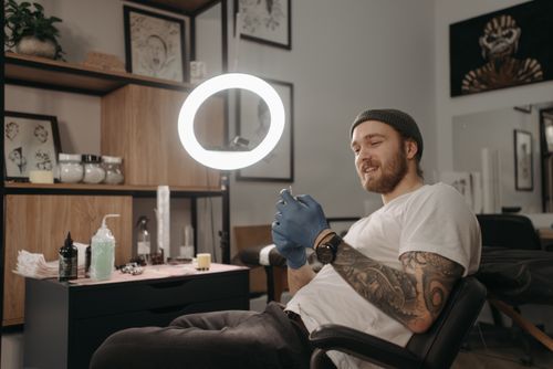 Free A tattoo artist wearing gloves relaxes in a parlor, surrounded by art and equipment. Stock Photo