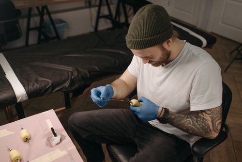 Free Tattoo artist with sleeve tattoo, adjusting tattoo machine in parlor setting. Stock Photo