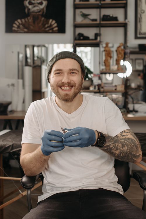 Free A cheerful tattoo artist with gloves in a lively studio setting, showcasing his tattoo equipment. Stock Photo