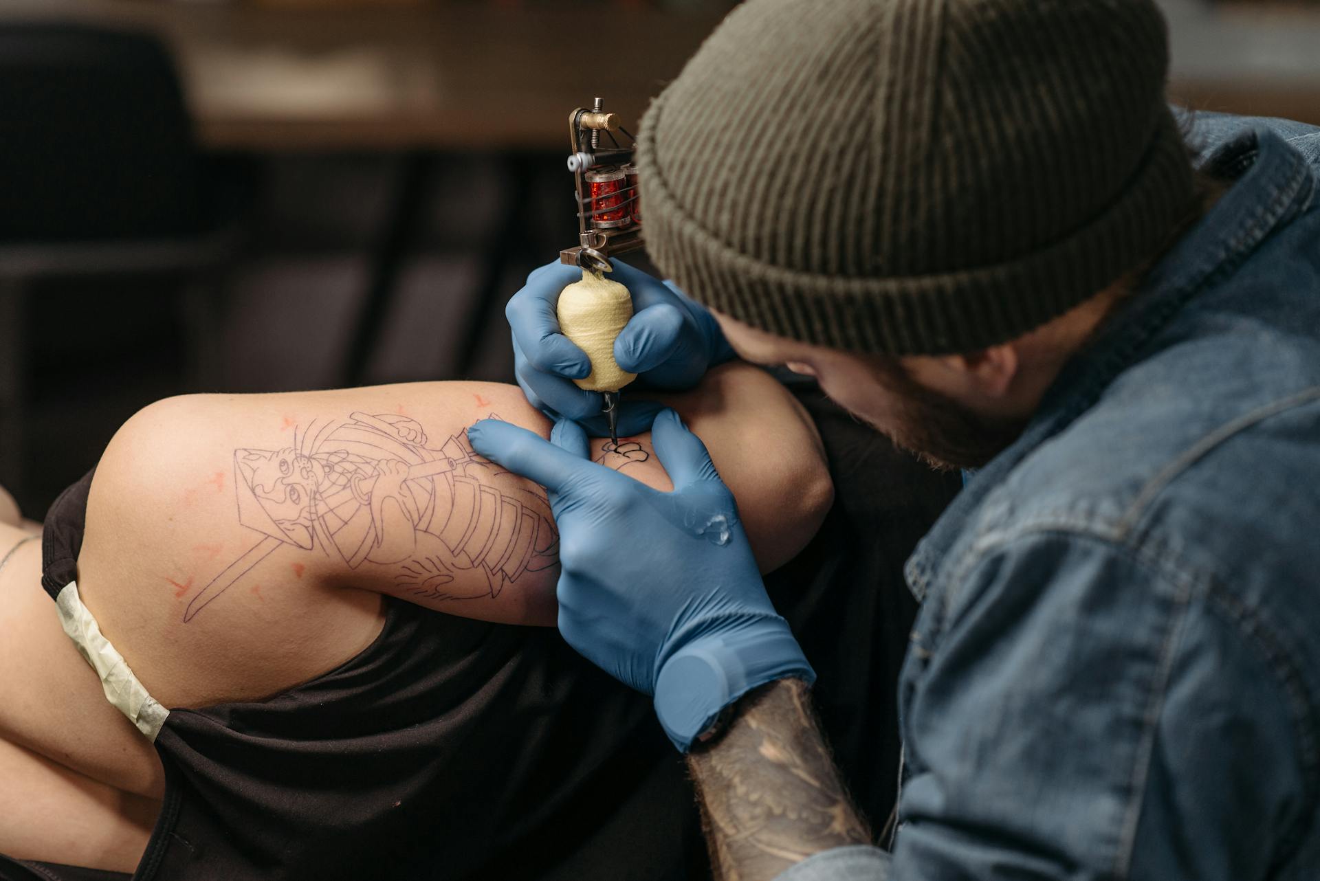 A tattoo artist inks an intricate design on a client's arm in a studio setting.