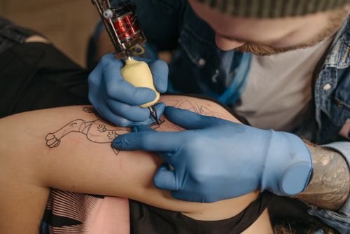 Free Tattoo artist using a machine to ink a client's arm with precision and skill in a studio setting. Stock Photo