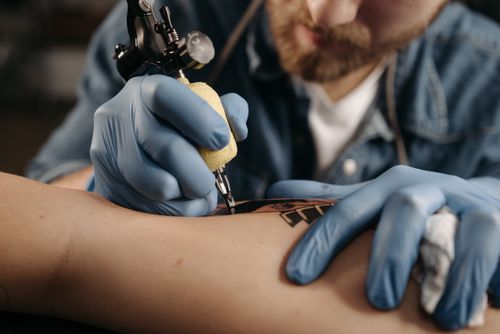 Free Tattoo artist working diligently on intricate design with tattoo machine and latex gloves. Stock Photo