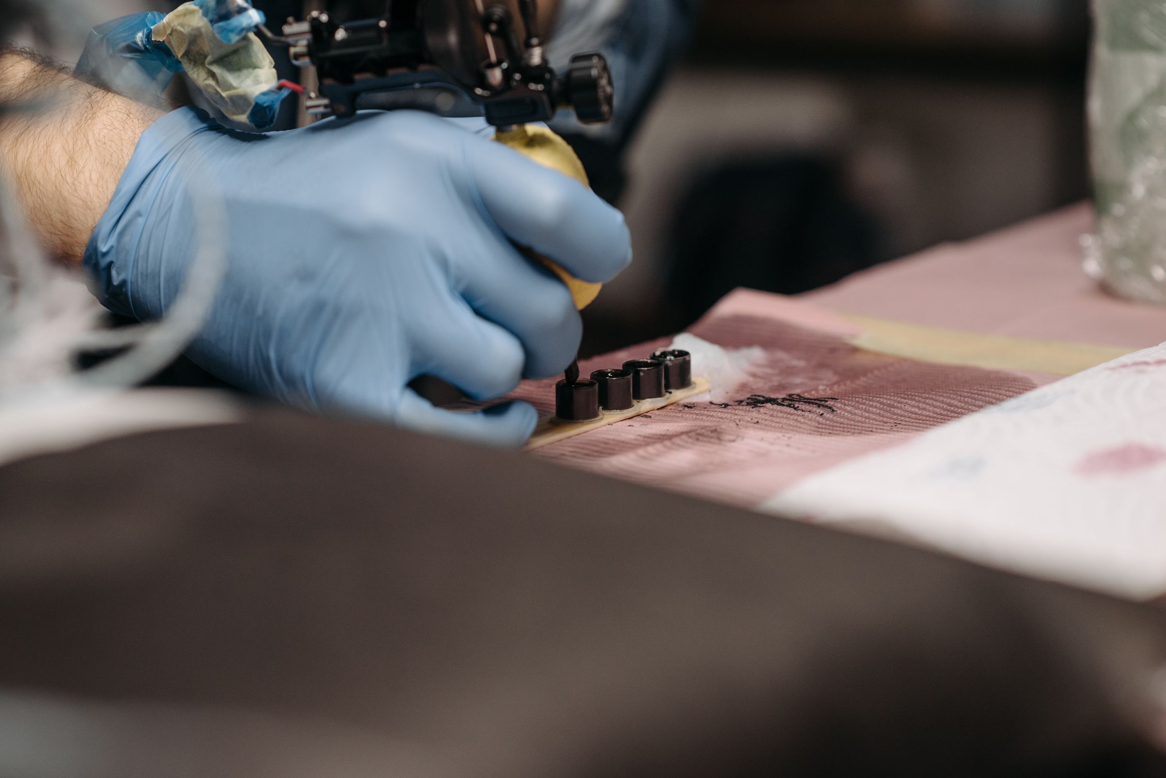 Gloved hand holding a tattoo machine, dipping into ink caps