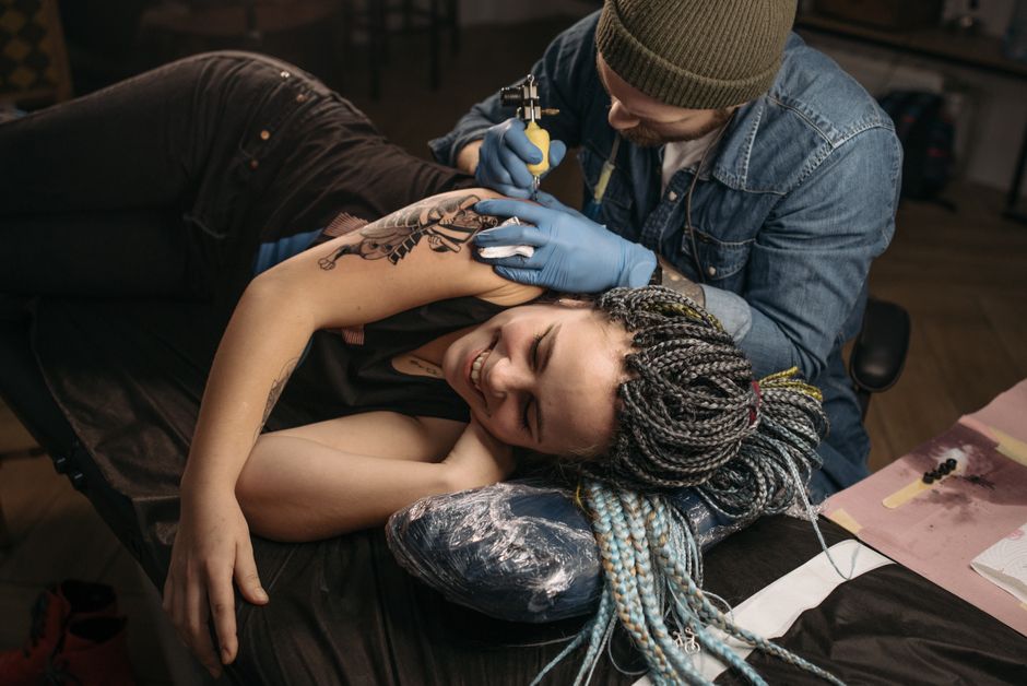 A relaxed tattoo client resting comfortably while a Tattoo Artist works on a detailed piece A relaxed tattoo client resting comfortably while a Tattoo Artist works on a detailed piece
