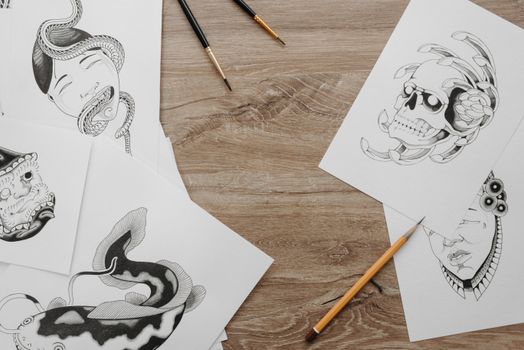 Creative sketch designs and drawing tools neatly arranged on a wooden table in a flat lay setup.