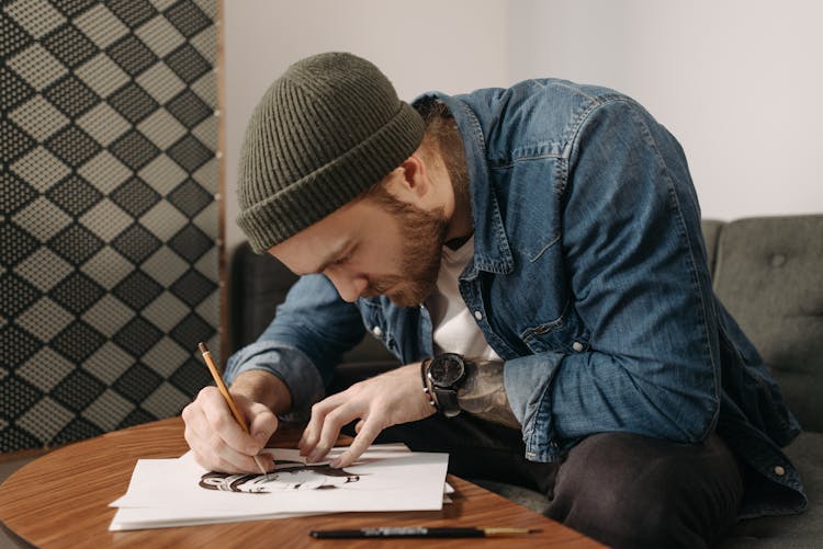 A Man In A Denim Jacket Drawing With A Pencil