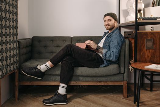 Man in casual attire sits on a stylish green sofa, using a tablet in a cozy indoor setting.