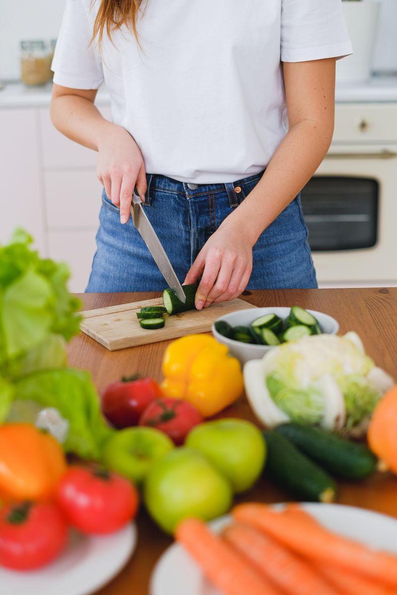 Woman slicing cucumbers surrounded by fresh vegetables