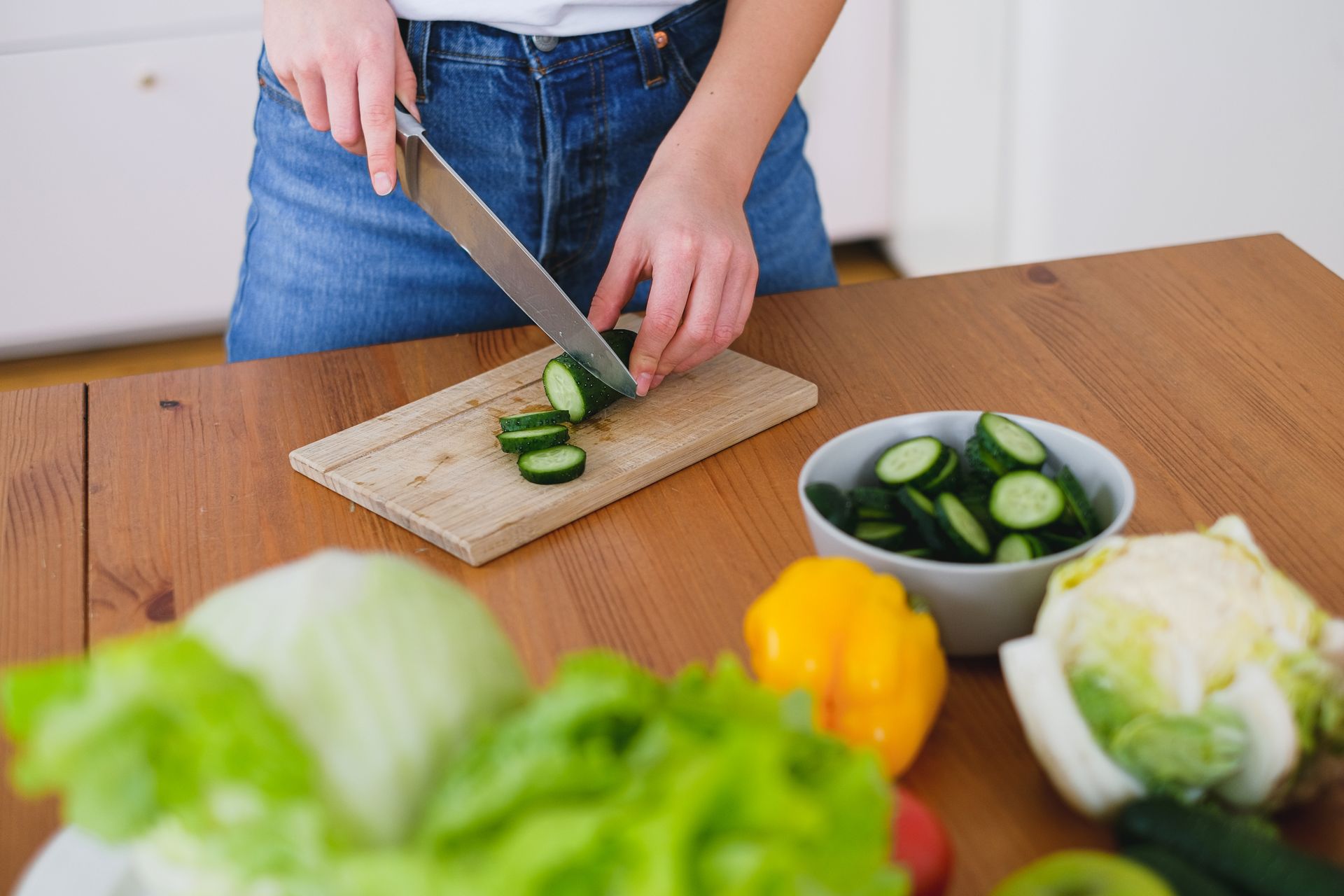 Healthy food preparation with fresh cucumbers and vegetables on a wooden table.