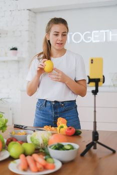 Woman streaming a cooking tutorial with vegetables and smartphone setup.