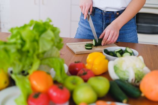 Woman slicing cucumbers surrounded by fresh produce in a bright kitchen setting.