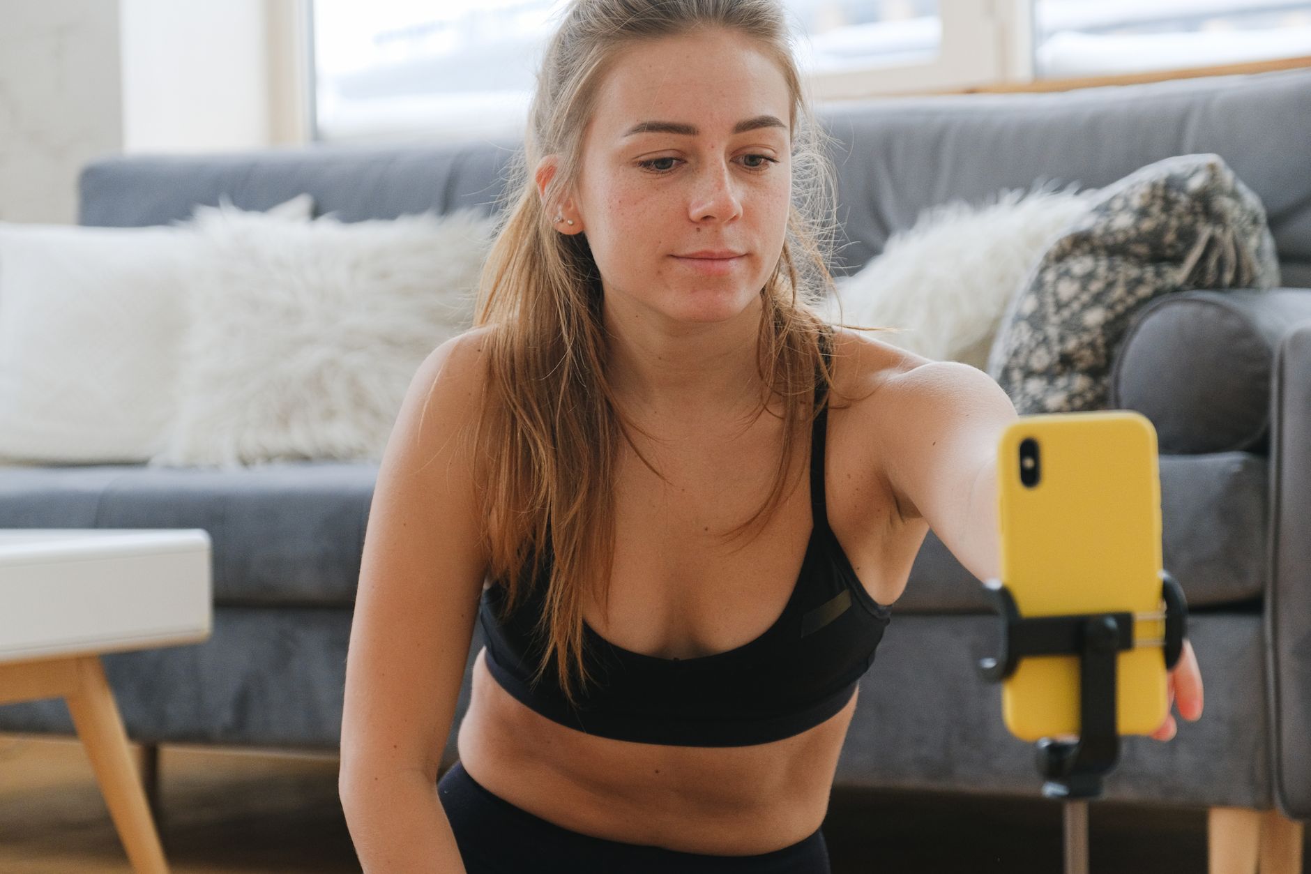 Young woman vlogging indoors, using smartphone on tripod. Casual and relaxed setting.