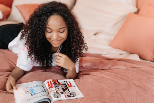Smiling Girl Lying Down on Bed and Reading Magazine
