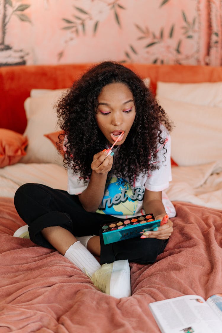 Woman Putting Lipstick While Sitting On Bed 