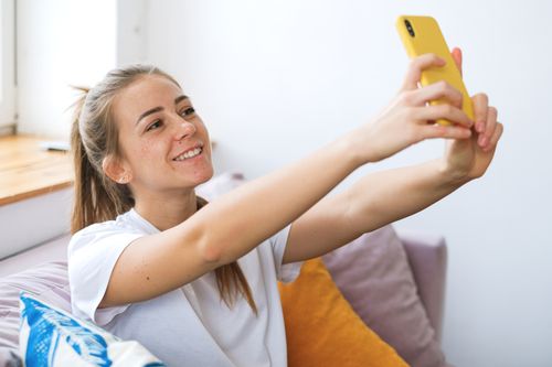 Free Smiling woman taking a selfie indoors with a yellow phone, relaxed at home. Stock Photo