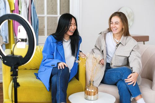 Free Two women laughing and recording a vlog indoors with a ring light and smartphone. Stock Photo