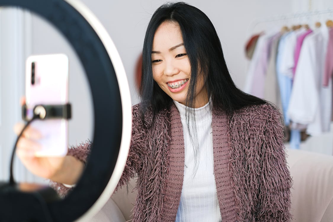 Free Smiling woman using smartphone and ring light for live streaming indoors. Stock Photo